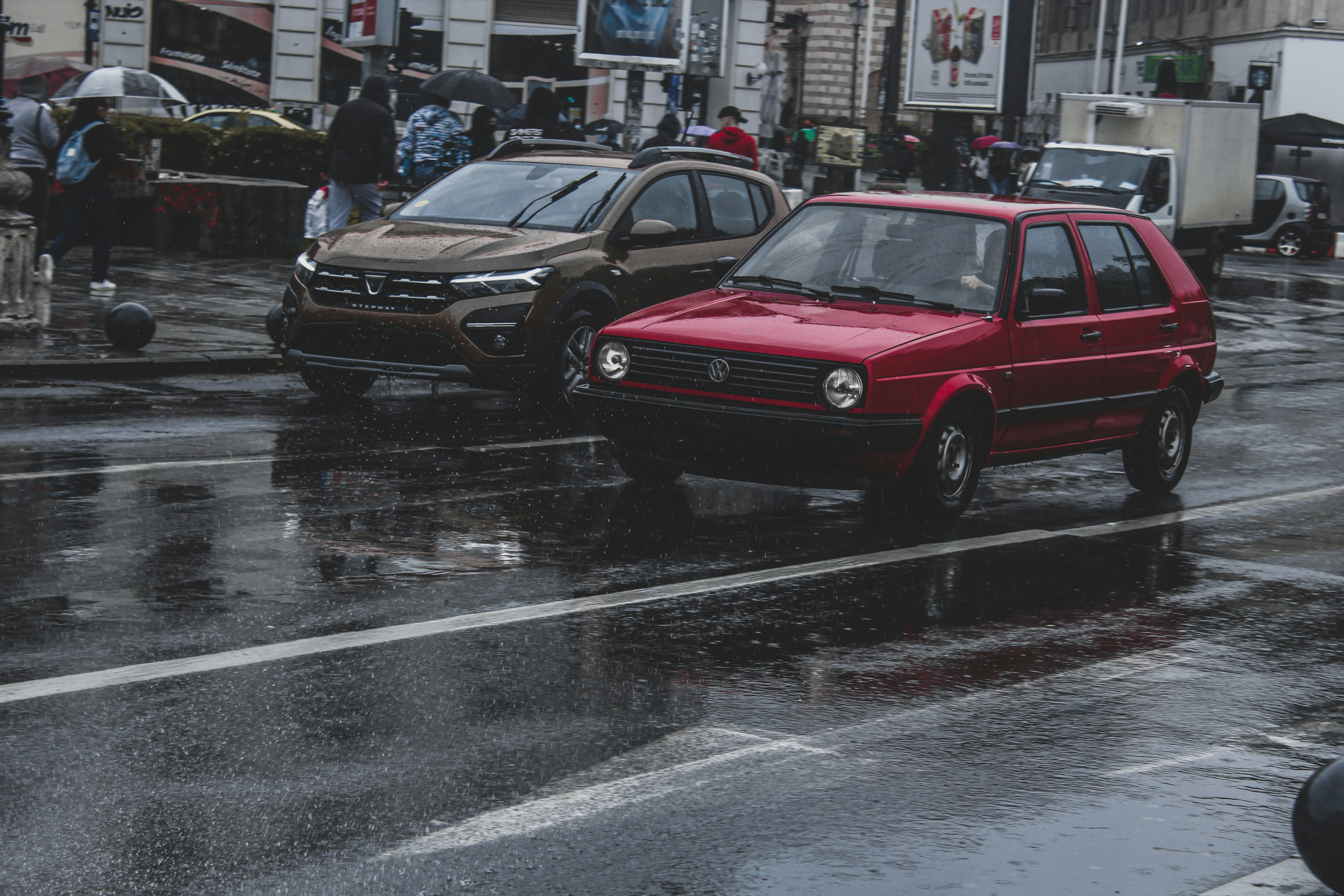 a red car driving down a rain soaked street
