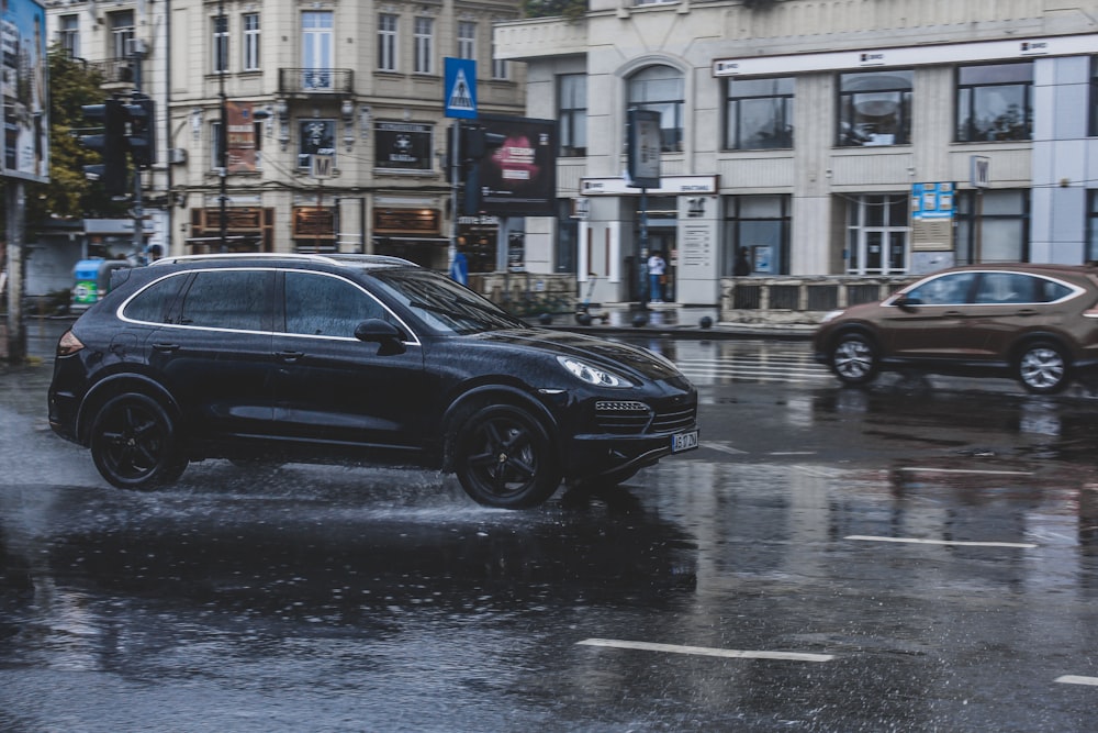 a black porsche cayen driving down a rain soaked street