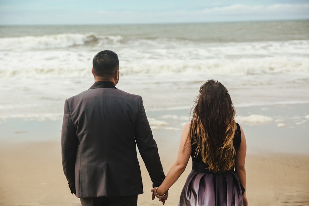 a man and a woman walking on the beach holding hands