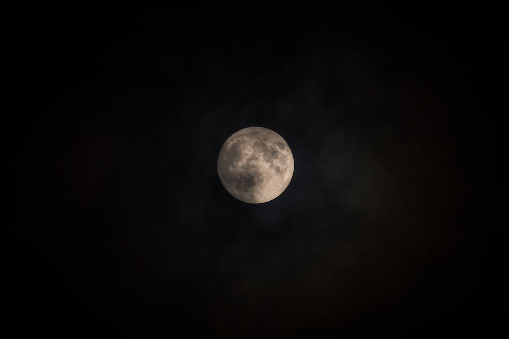 a full moon seen through the clouds in a dark sky