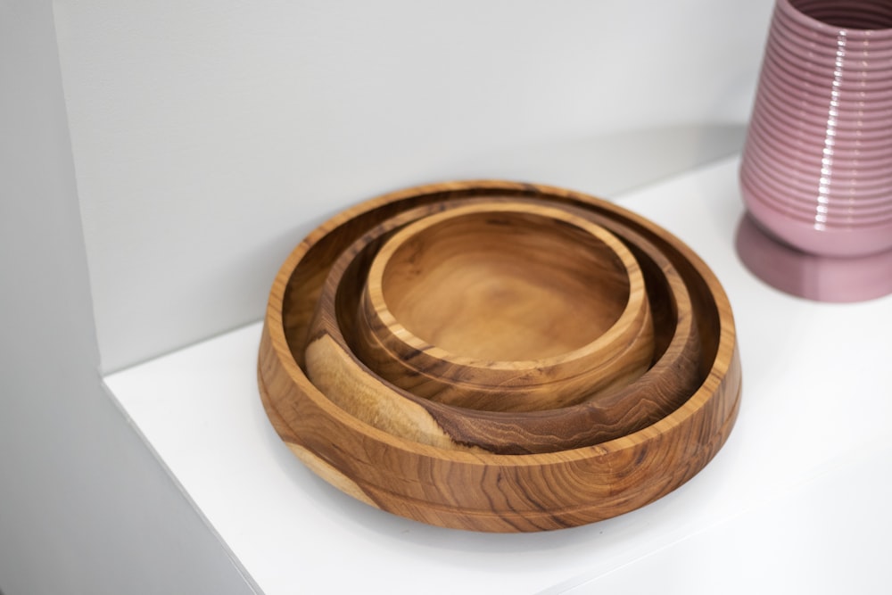 three wooden bowls sitting on a shelf next to a pink vase