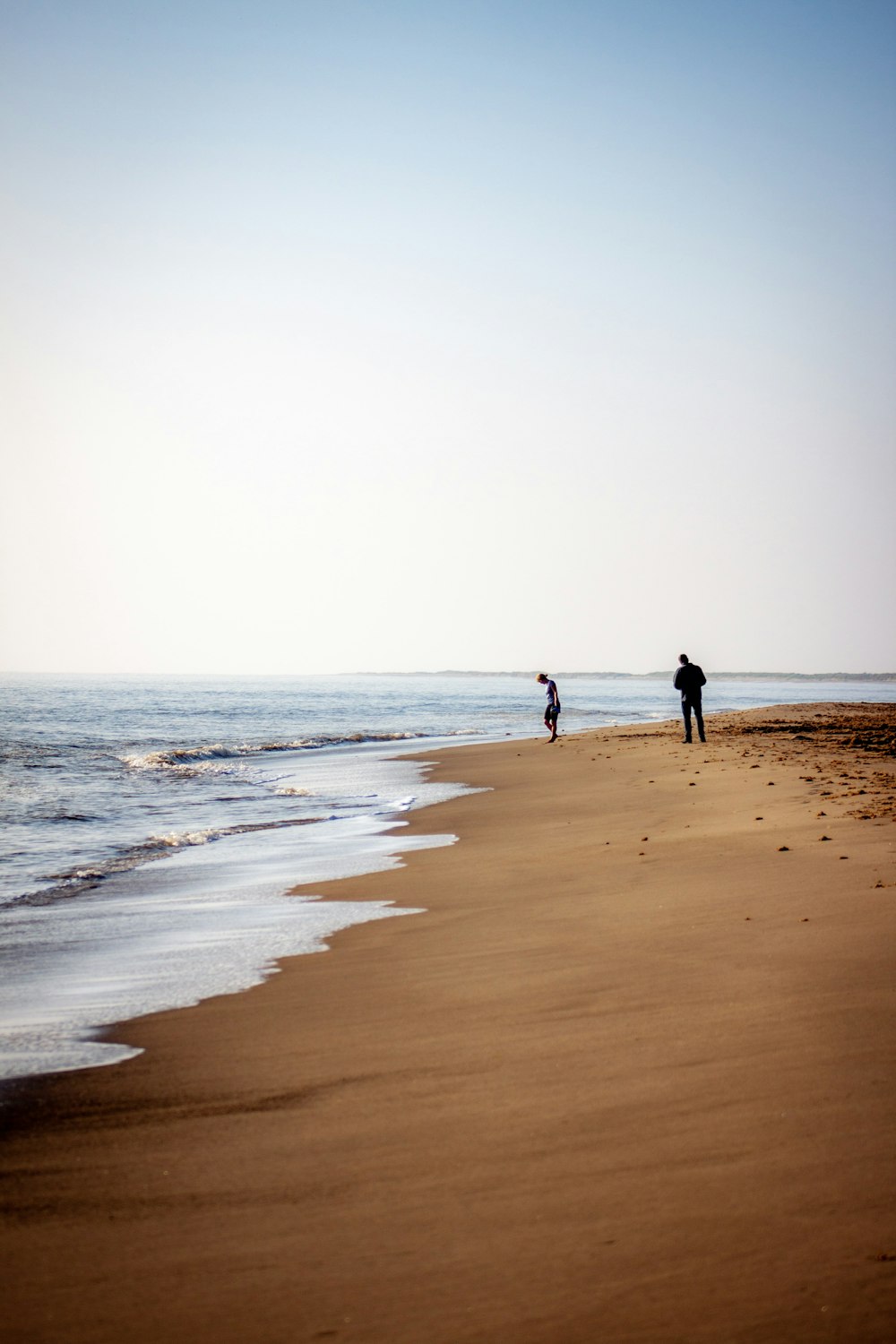 a couple of people standing on top of a sandy beach