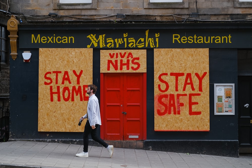a man walking past a mexican restaurant with boarded up doors