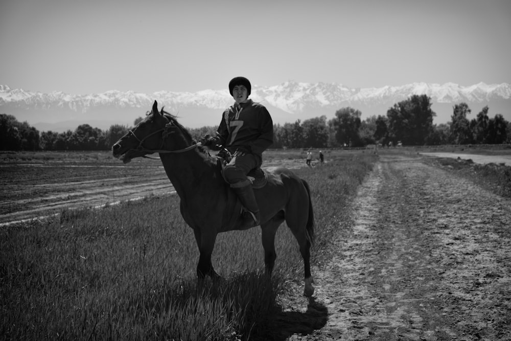a man riding on the back of a horse down a dirt road