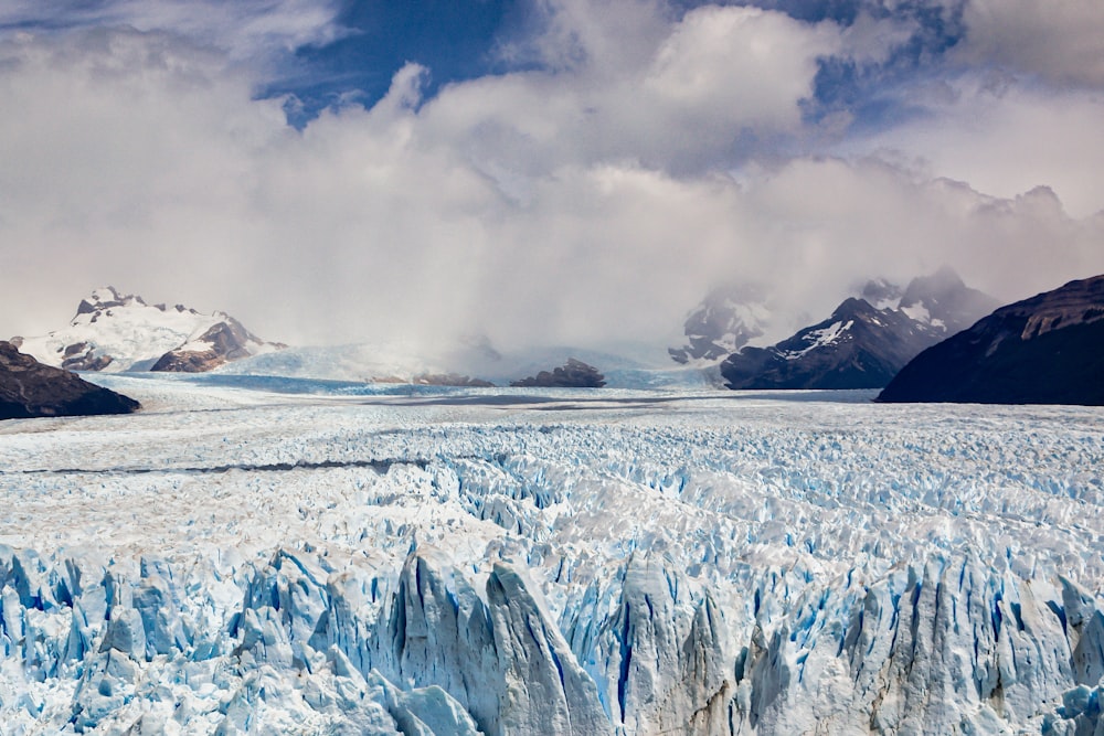 a large glacier surrounded by mountains under a cloudy sky