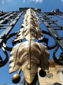 Close-up of a metal fence gate with intricate design details, shining under the sun.