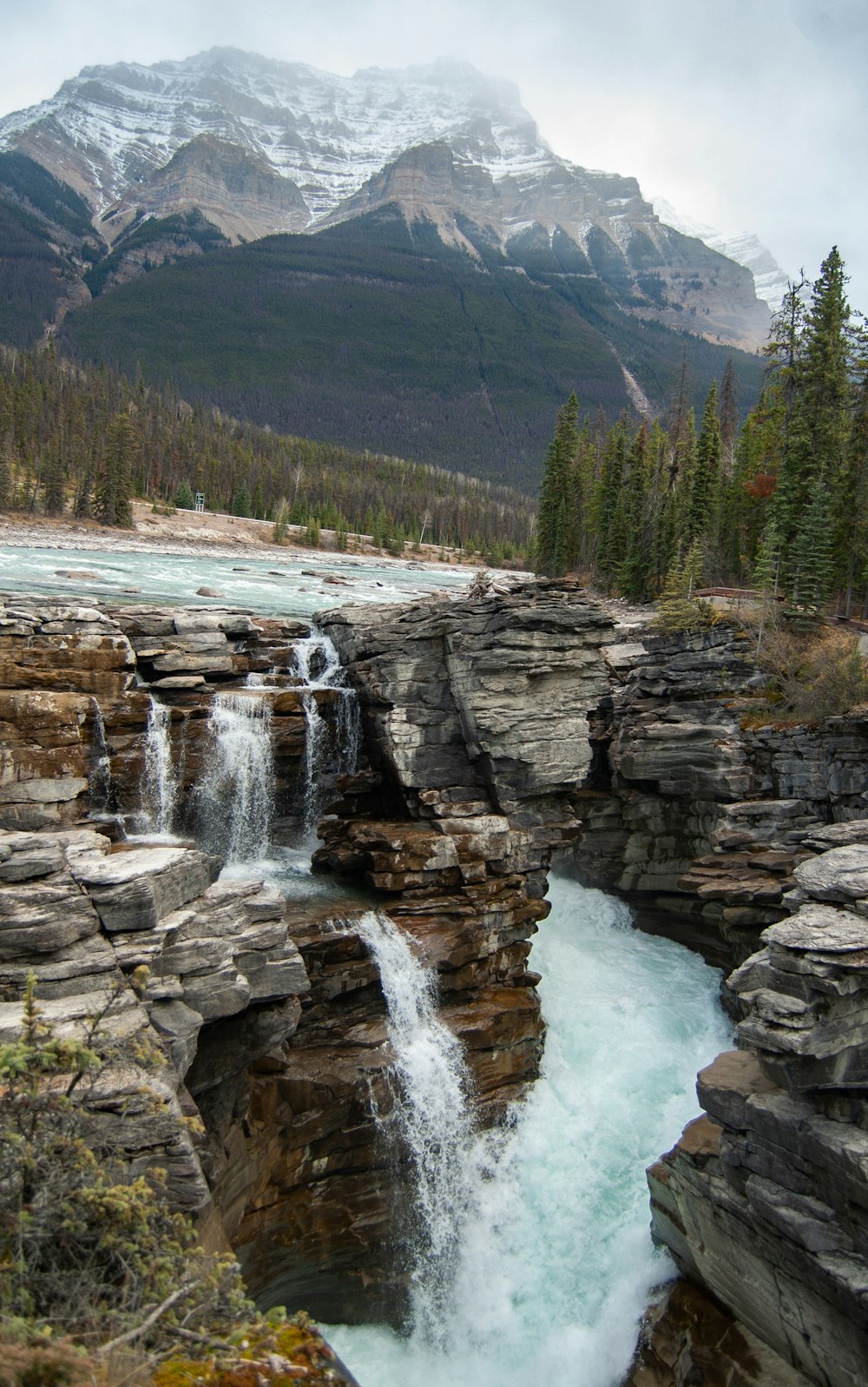 a waterfall in the middle of a river surrounded by mountains