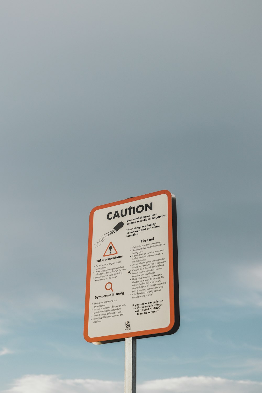 a caution sign on a pole in front of a cloudy sky