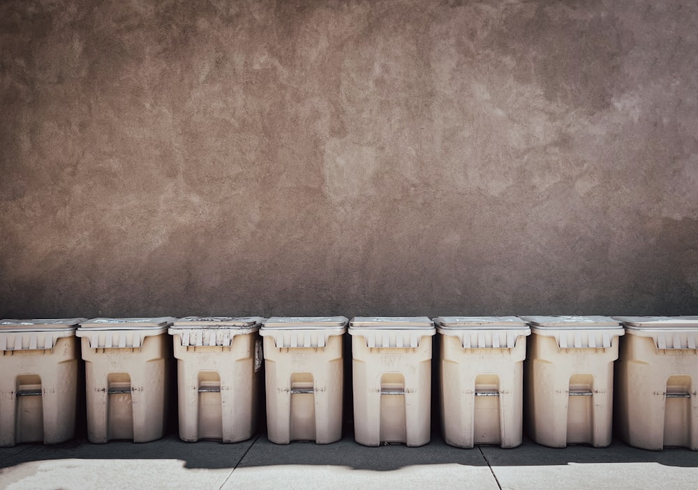 a row of white trash cans sitting next to a wall