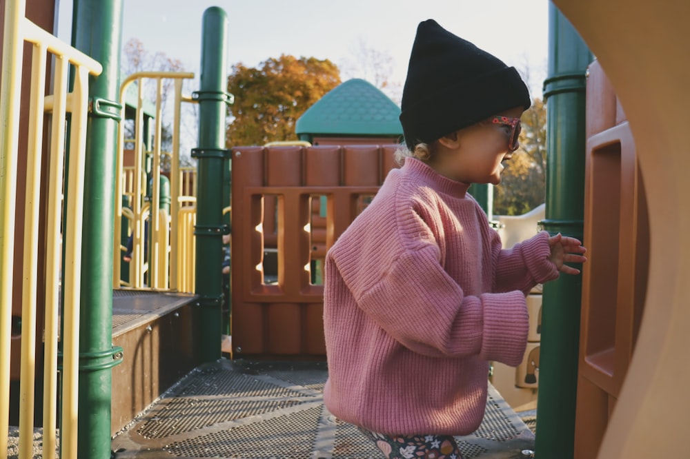 a little girl in a pink sweater playing on a playground