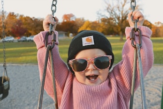 a little girl wearing sunglasses and a hat on a swing