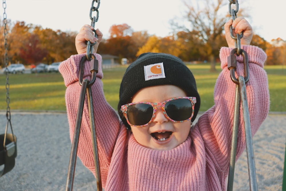 a little girl wearing sunglasses and a hat on a swing
