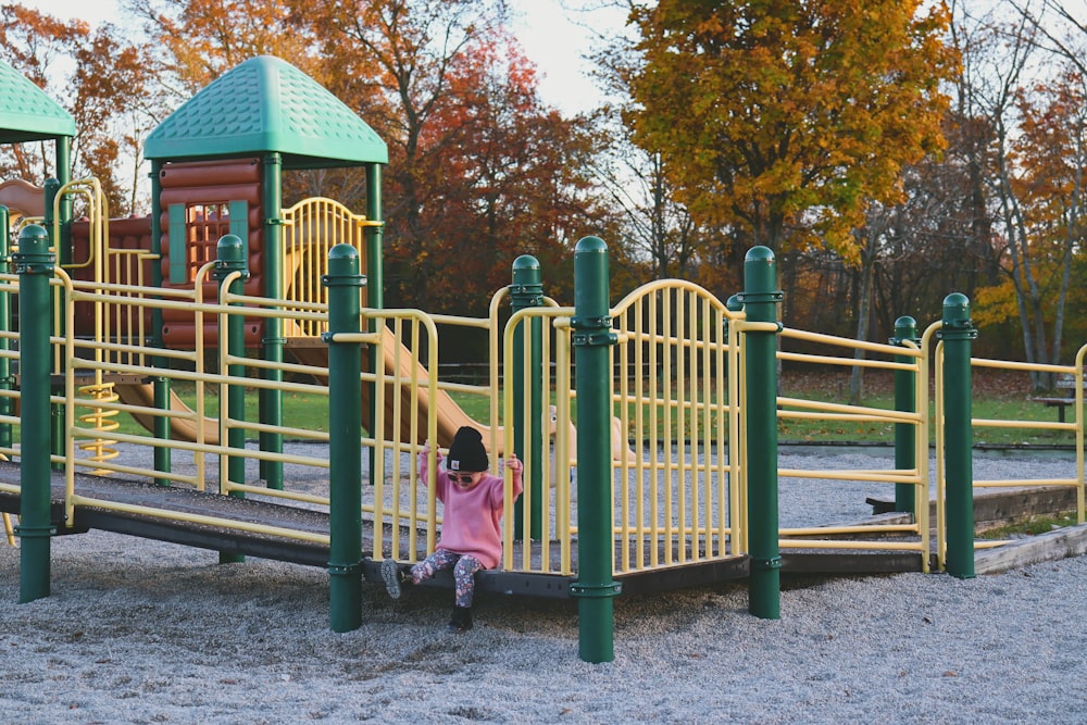 a little girl playing on a yellow and green playground