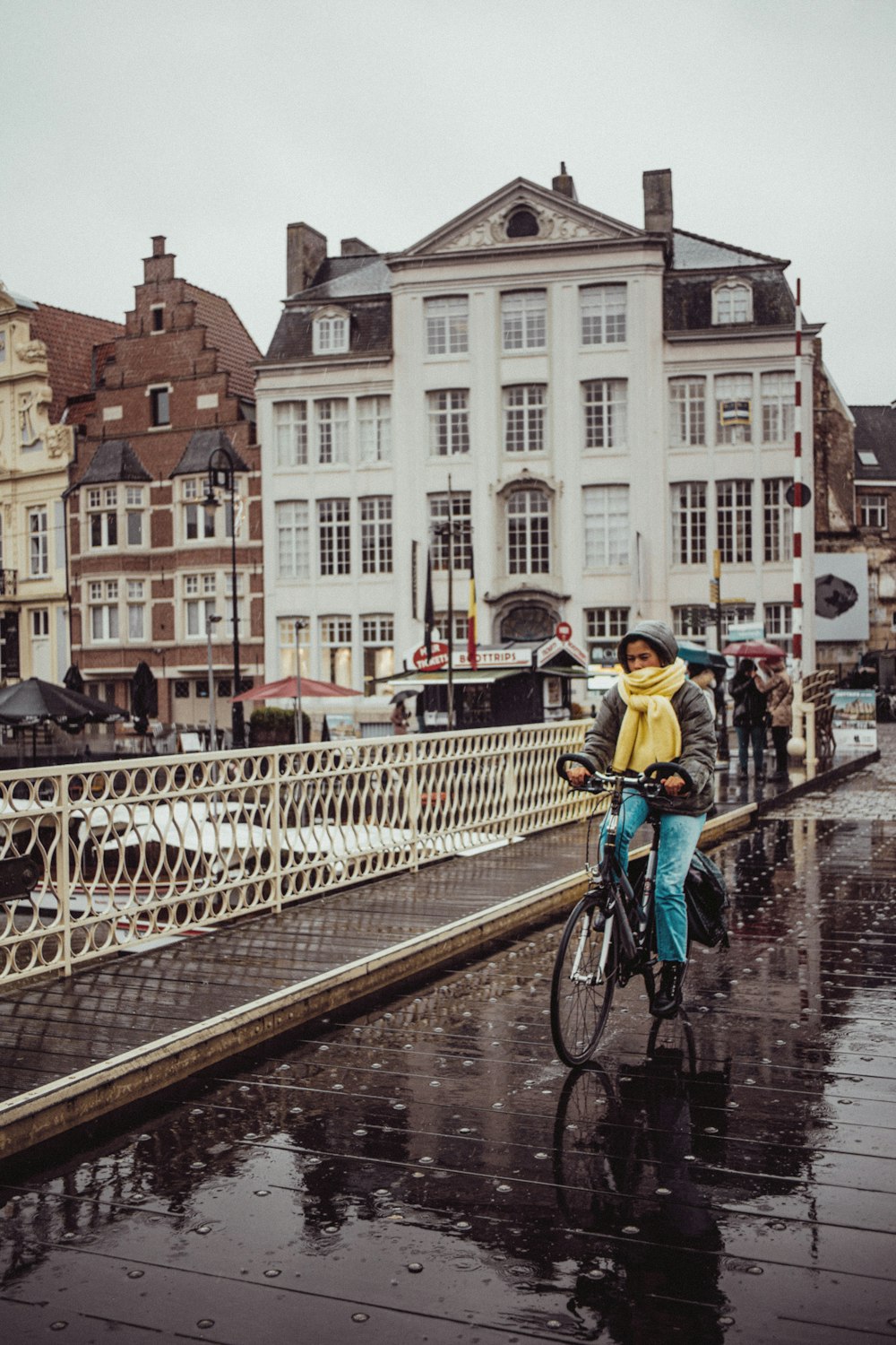 a woman riding a bike across a bridge in the rain