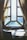 A wooden table and chairs are positioned in front of a large, finely crafted window with multiple panes, framed by elegant, draped curtains. Sunlight streams in, casting soft, diffused shadows on the table and creating an inviting and warm atmosphere.