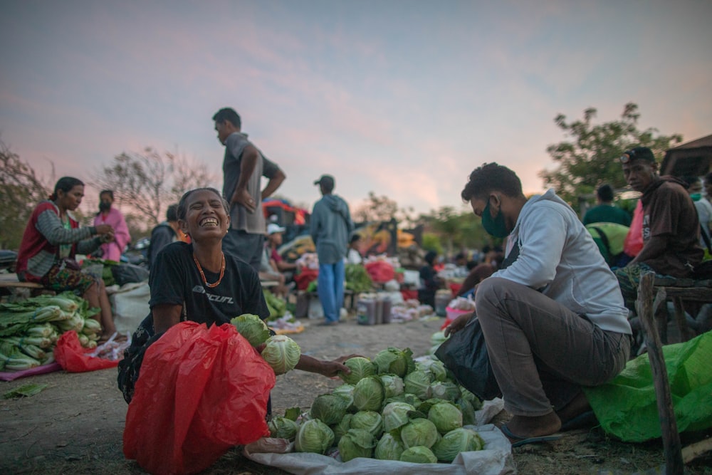 a group of people sitting around a pile of vegetables