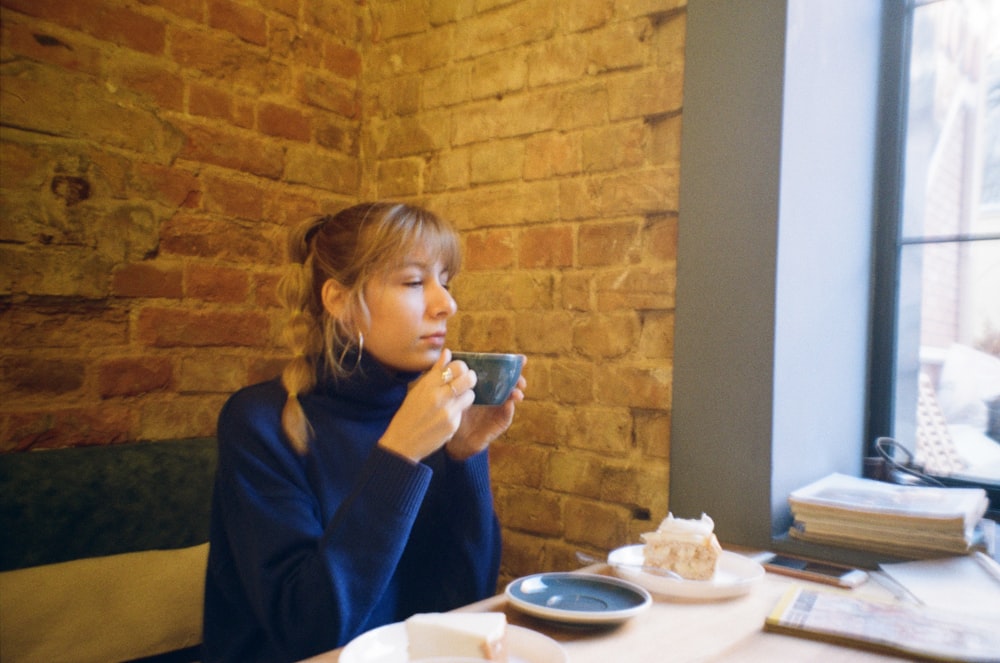a woman sitting at a table drinking a cup of coffee