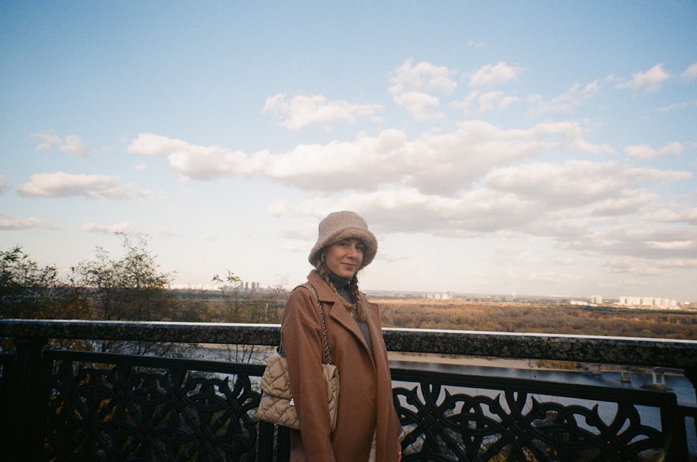 a woman in a brown coat and hat standing on a balcony