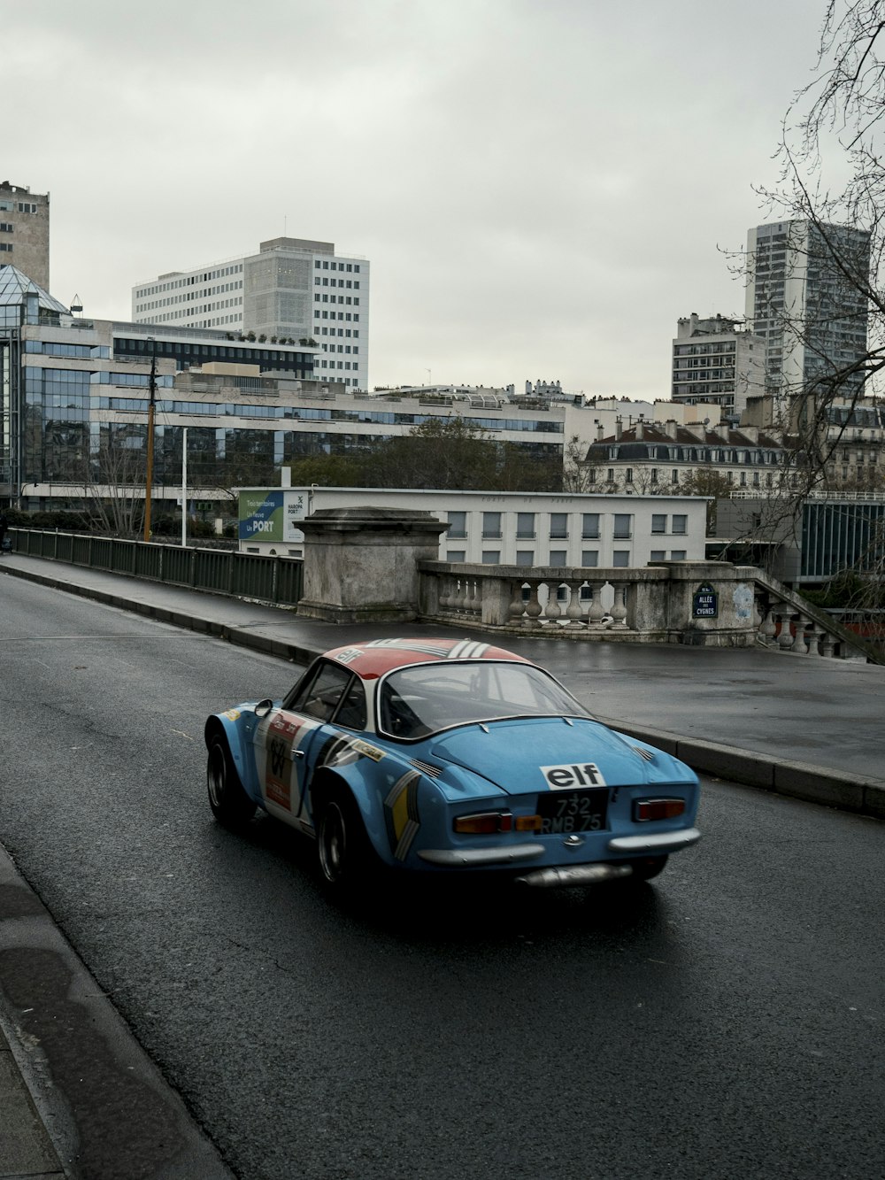 a blue car driving down a street next to tall buildings