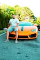 a man sitting on top of an orange sports car
