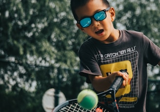 a young boy holding a tennis racquet on top of a tennis court