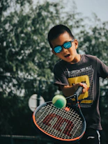 a young boy holding a tennis racquet on top of a tennis court