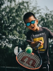 a young boy holding a tennis racquet on top of a tennis court