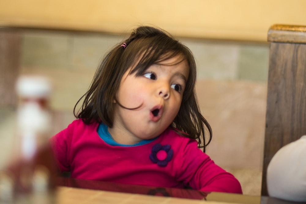 a little girl sitting at a table with a surprised look on her face