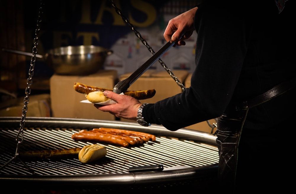 a person holding a knife over some hot dogs on a grill