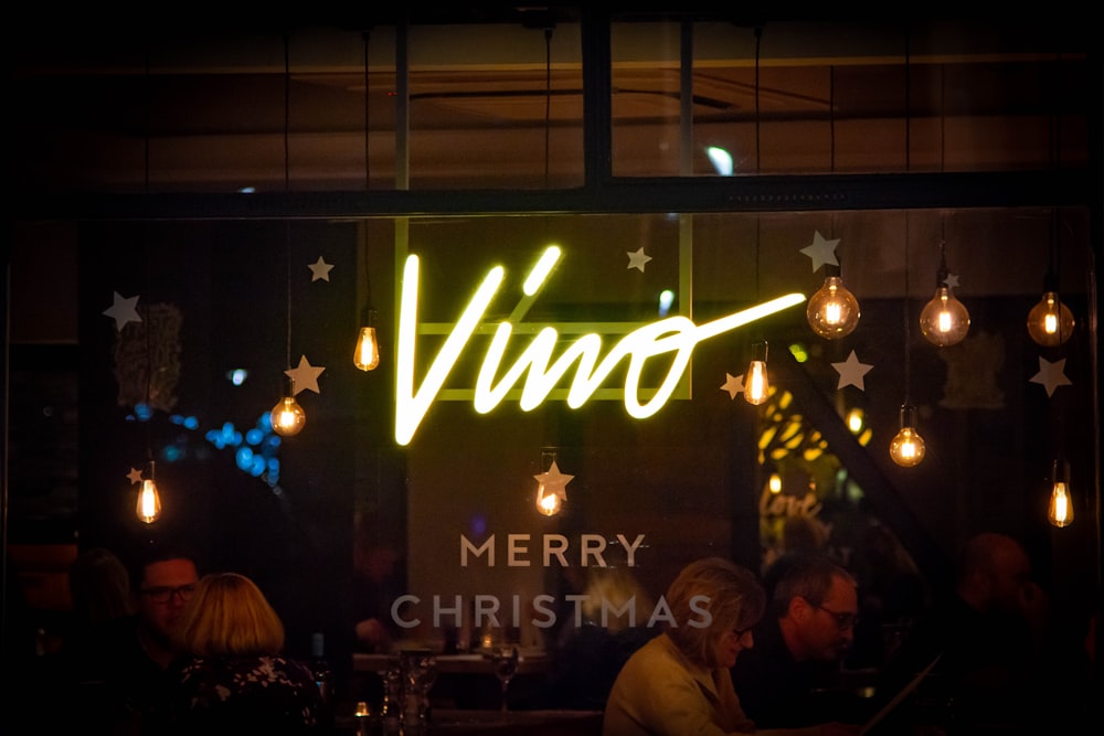 a group of people sitting at a table in front of a neon sign