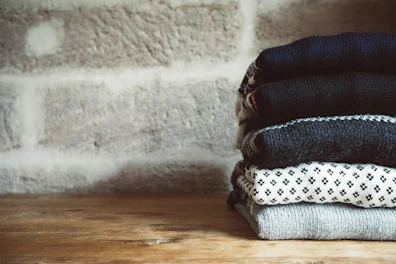 A neat stack of folded cotton sweaters in soft pastel shades on a wooden table.