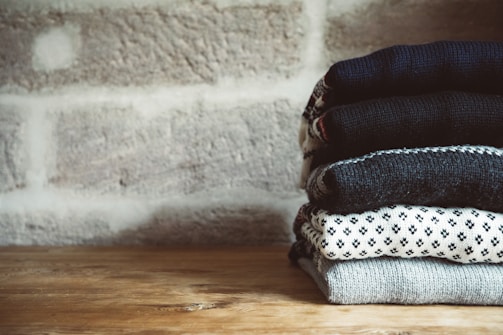 Neatly folded sweaters arranged on wooden shelves in a workspace.