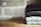 A stack of neatly folded sweaters with various patterns and colors resting on a wooden surface against a textured brick wall.