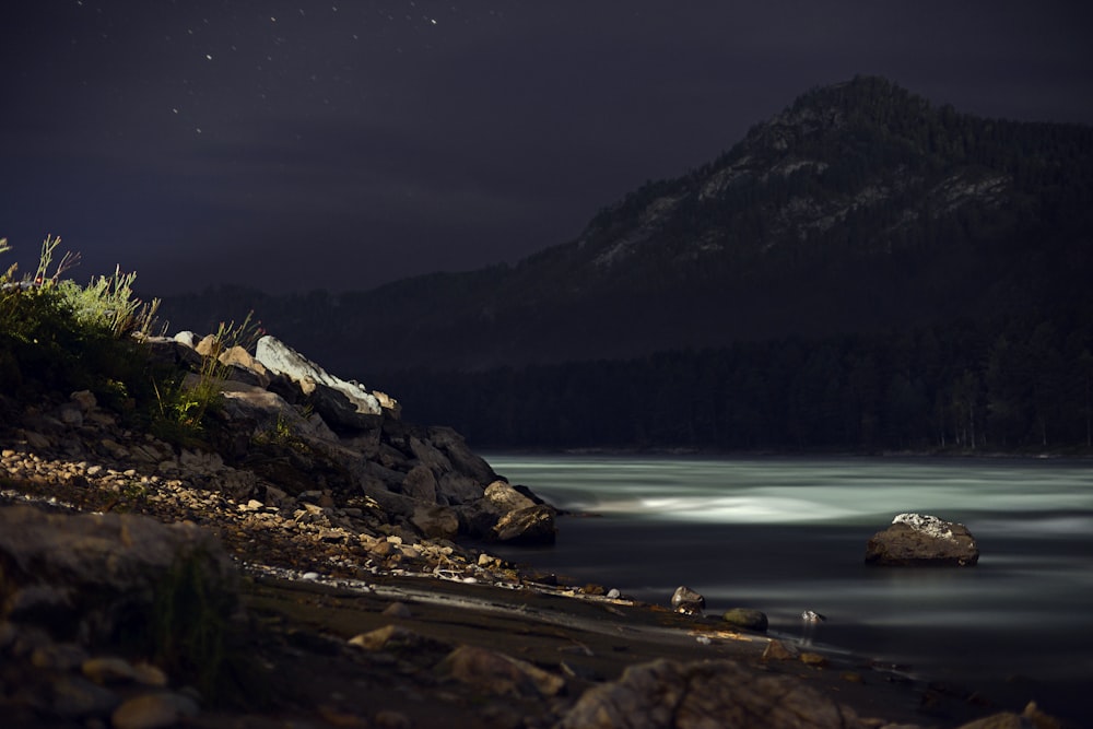 a body of water at night with a mountain in the background
