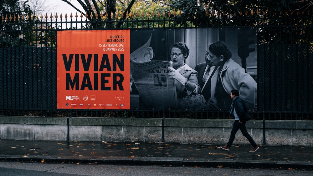 a man walking down a street past a large poster