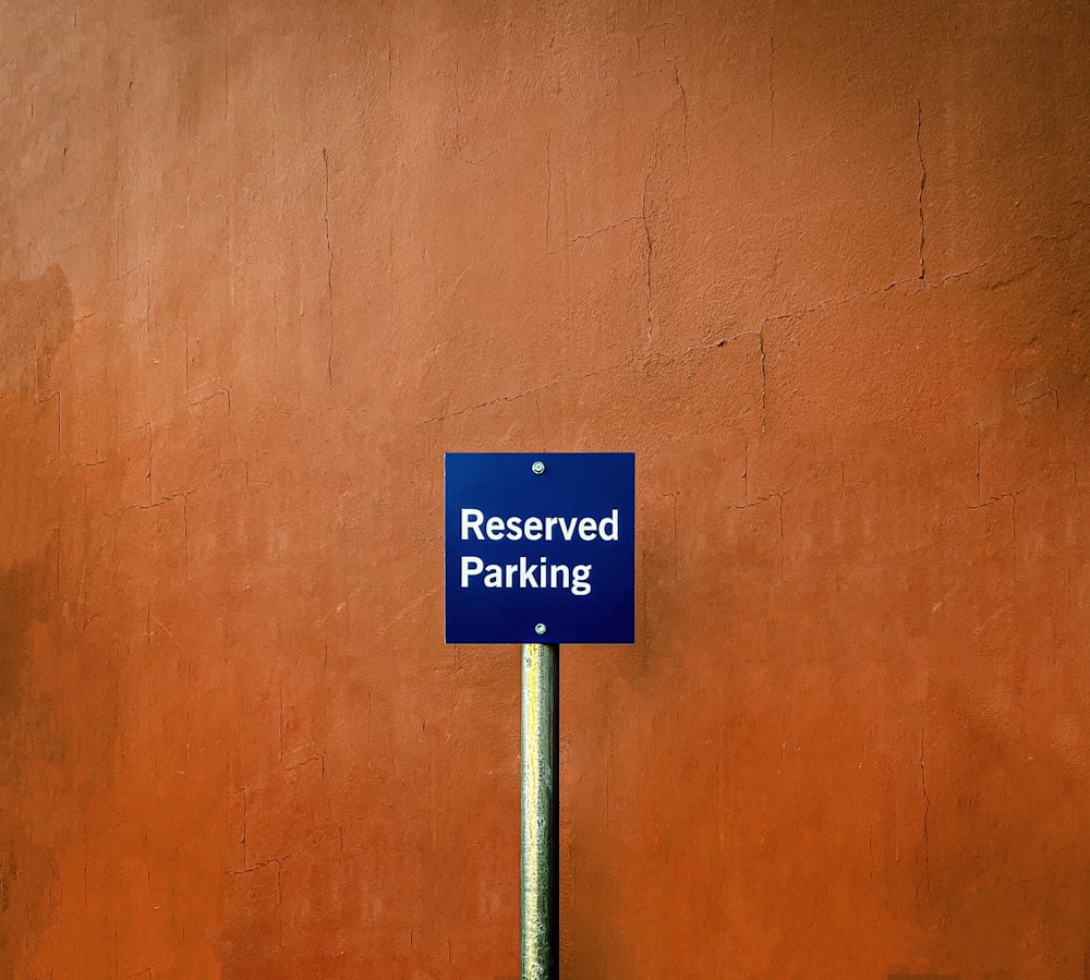 a blue sign that reads reserved parking in front of a red wall