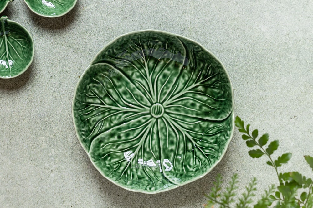 a green bowl sitting on top of a table next to a plant