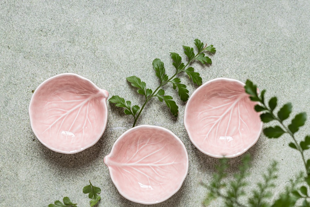 three pink bowls with green leaves on them