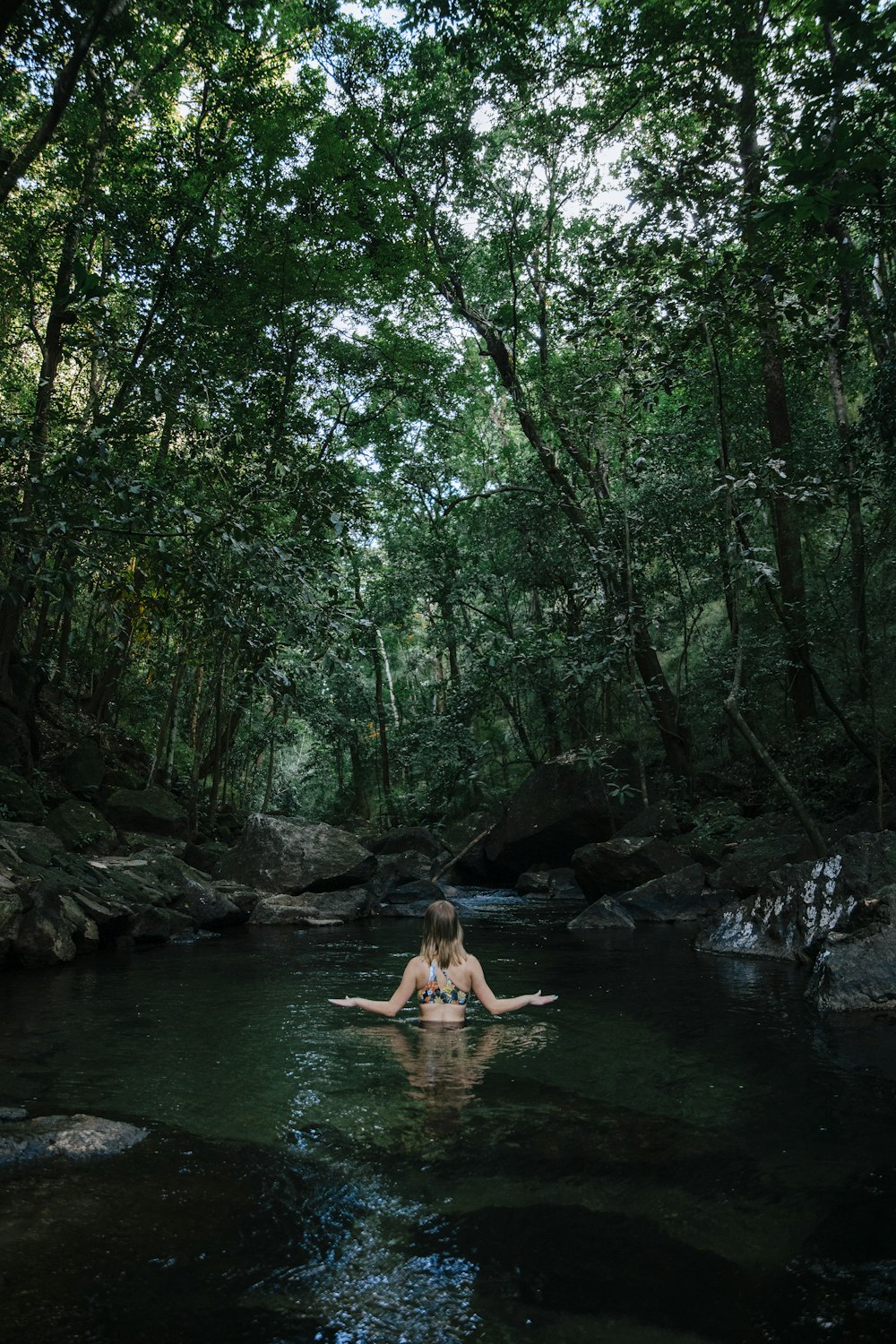 a woman sitting in a river surrounded by trees