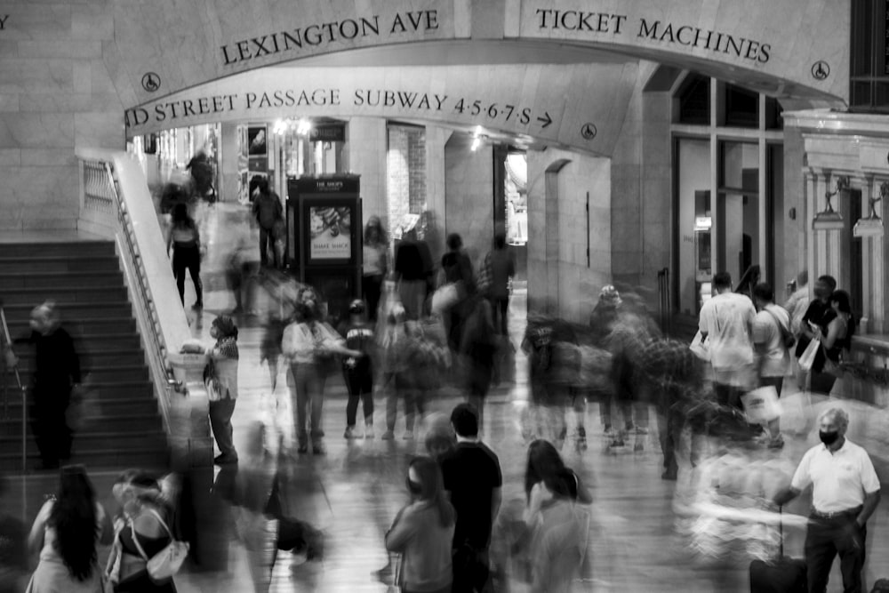a black and white photo of people walking in front of a ticket machine