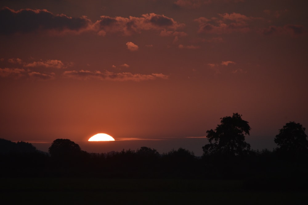 the sun is setting over a field with trees