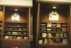 A display of clothing and accessories in a wooden cabinet, featuring neatly arranged shirts, ties, and boxes. The left side showcases a blue button-up shirt with a patterned tie, while the right side displays a light-colored shirt with a blue bow tie. Below are shelves with various patterned and colored ties, and some boxed items.