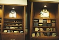 A display of clothing and accessories in a wooden cabinet, featuring neatly arranged shirts, ties, and boxes. The left side showcases a blue button-up shirt with a patterned tie, while the right side displays a light-colored shirt with a blue bow tie. Below are shelves with various patterned and colored ties, and some boxed items.