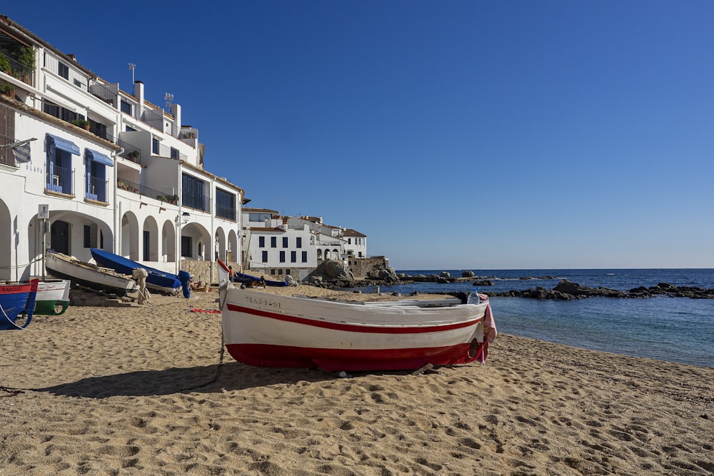 a red and white boat sitting on top of a sandy beach