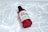 A red-capped bottle labeled 'Snail Truecica Miracle Repair Serum' lies on a surface with a pattern resembling light reflections on water. The bottle is clear with red accents, containing a dark liquid inside.