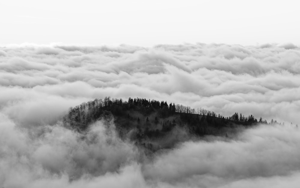 a black and white photo of a mountain surrounded by clouds