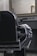 A classic black leather barber chair with shiny metal details is positioned in front of a countertop holding grooming tools. A striped barber cape is draped over the chair's armrest. A large, ornate mirror hangs above the countertop in a room with subdued lighting, reflecting part of the room.