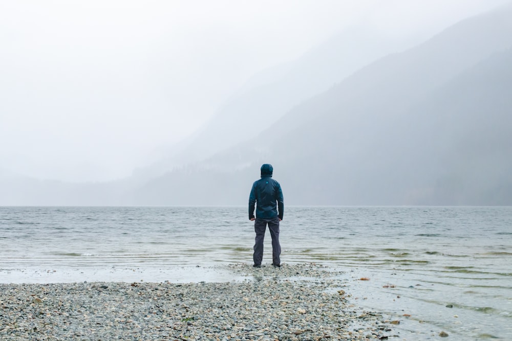 a man standing on a rocky beach next to a body of water