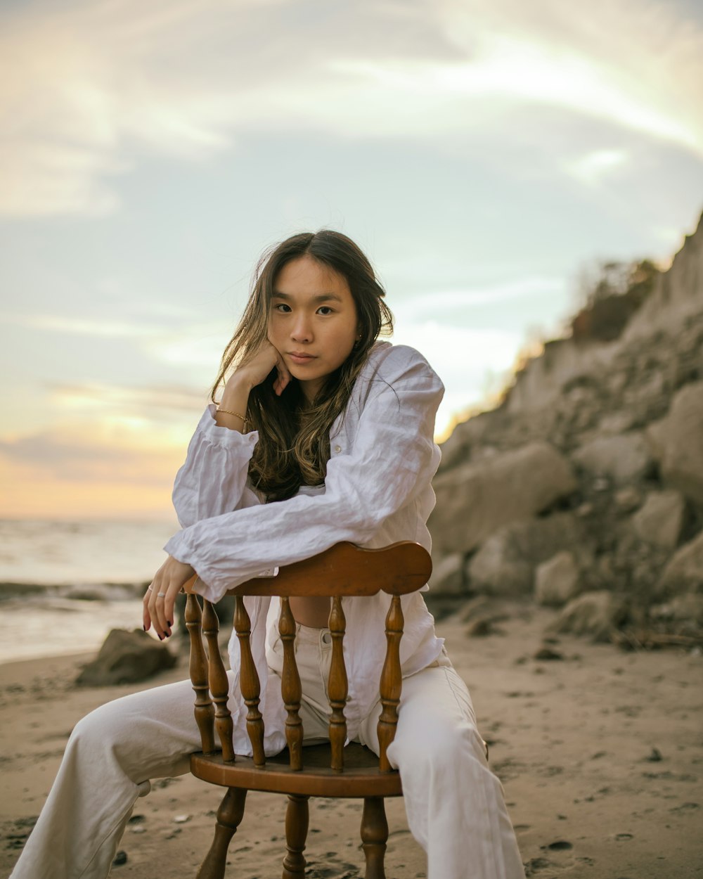 a woman sitting on top of a wooden chair on a beach