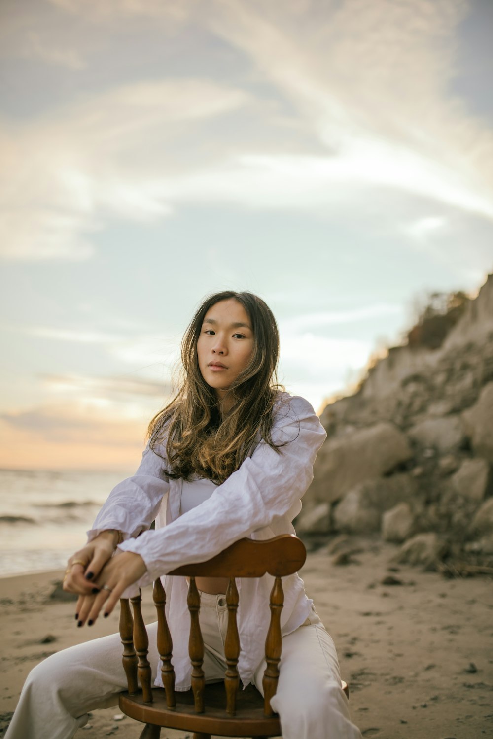 a woman sitting on top of a wooden chair on a beach